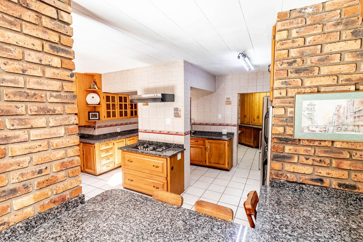 Spacious kitchen featuring granite countertops, wooden cabinetry, gas hob with extractor, and exposed brick architectural elements, offering a functional layout with ample storage.