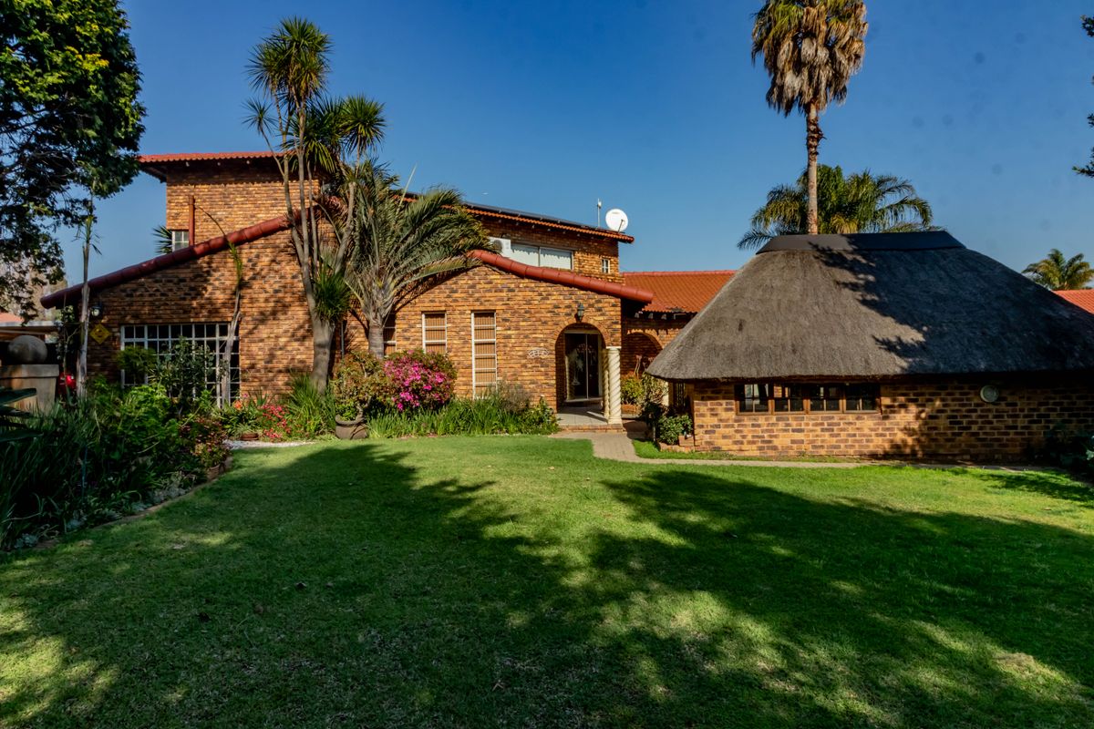 Rear view of a face brick house featuring a well-maintained garden, a thatched roof lapa, and a paved walkway leading to the main entrance.