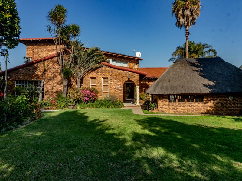 Rear view of a face brick house featuring a well-maintained garden, a thatched roof lapa, and a paved walkway leading to the main entrance.