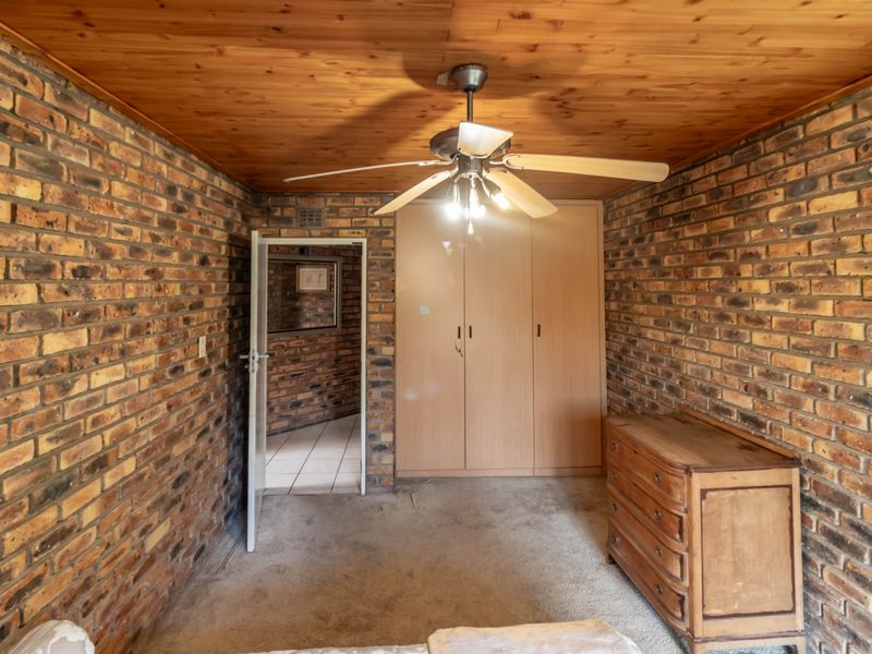 Bedroom featuring exposed brick walls, timber ceiling, built-in cupboards, and a ceiling fan, offering a rustic aesthetic ready for modernization.