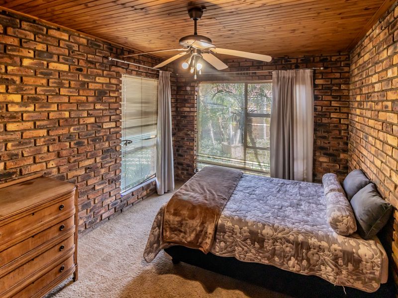A cozy bedroom featuring rustic exposed brick walls, a warm timber ceiling, and a functional ceiling fan, offering a unique character-filled living space.
