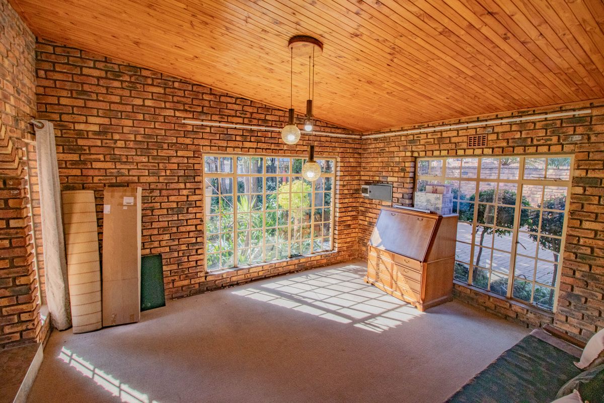 A spacious living area featuring exposed brick walls, a warm timber-clad vaulted ceiling, and large windows that provide ample natural light and garden views.
