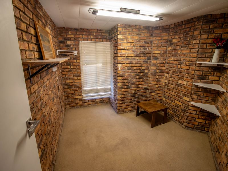 A bedroom featuring exposed brick walls, carpeted flooring, and built-in shelving, offering a rustic aesthetic ready for modernization.