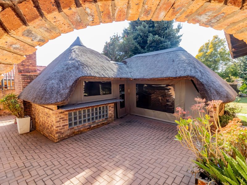 Outdoor entertainment area featuring a thatched roof structure, brick paving, and a built-in bar counter, perfect for alfresco dining and social gatherings.