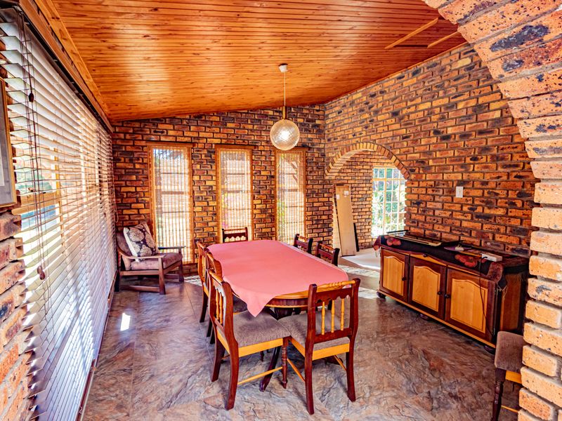 A dining room featuring exposed brick walls, a warm timber ceiling, tiled flooring, and an arched architectural opening leading to an adjacent space.