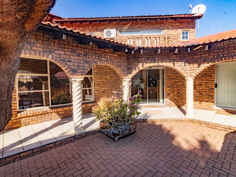 A spacious covered patio featuring classic brick arches, spiral columns, and tiled flooring, providing a charming outdoor entertainment area with direct access to the home.