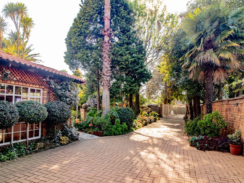 A well-maintained front entrance area featuring brick paving, established garden landscaping, and a classic brick facade with multi-pane windows.