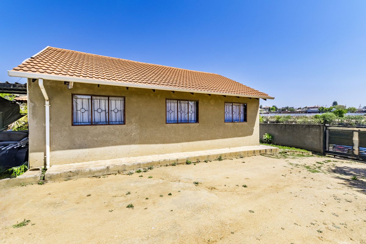 Rear view of the property featuring a terracotta tiled roof, security bars on windows, and a concrete perimeter wall in a spacious yard.