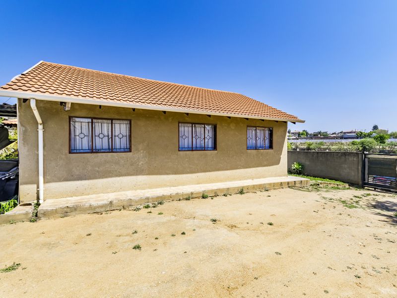 Rear view of the property featuring a terracotta tiled roof, security bars on windows, and a concrete perimeter wall in a spacious yard.