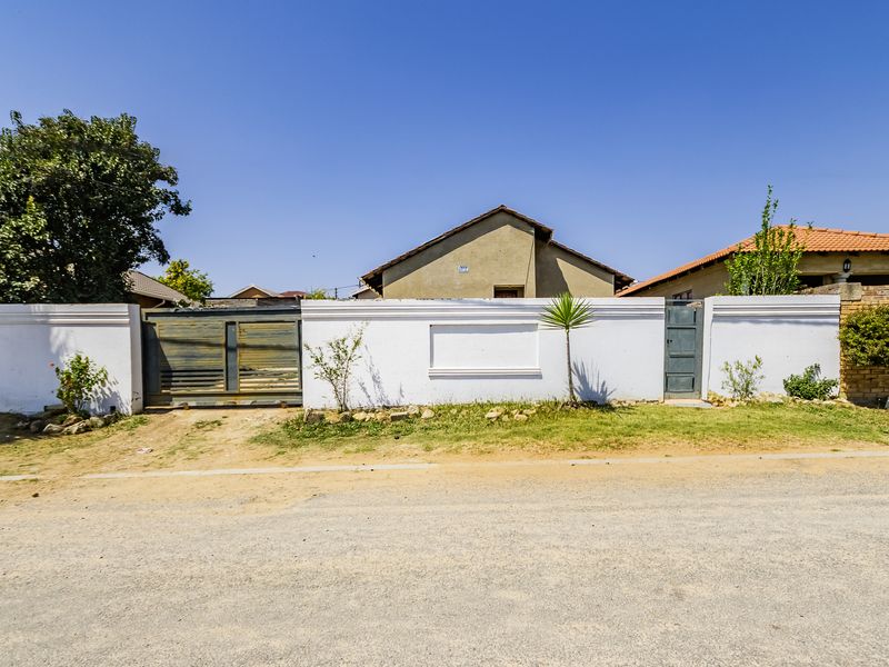 Front exterior view of the property featuring a perimeter wall, sliding driveway gate, and pedestrian access gate.