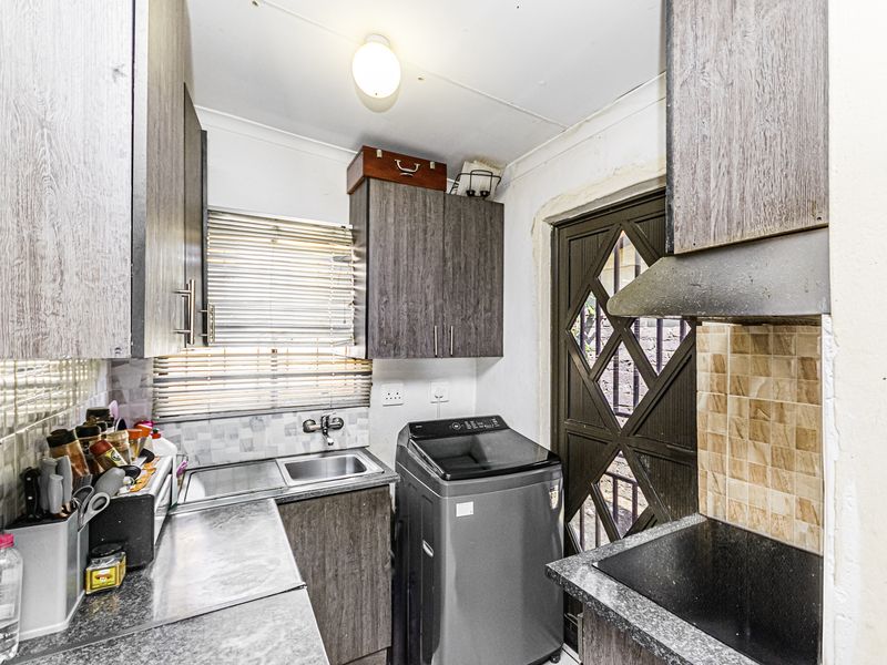 Compact scullery area featuring built-in cabinetry, a stainless steel sink, and a tiled backsplash, providing functional utility space with direct exterior access.