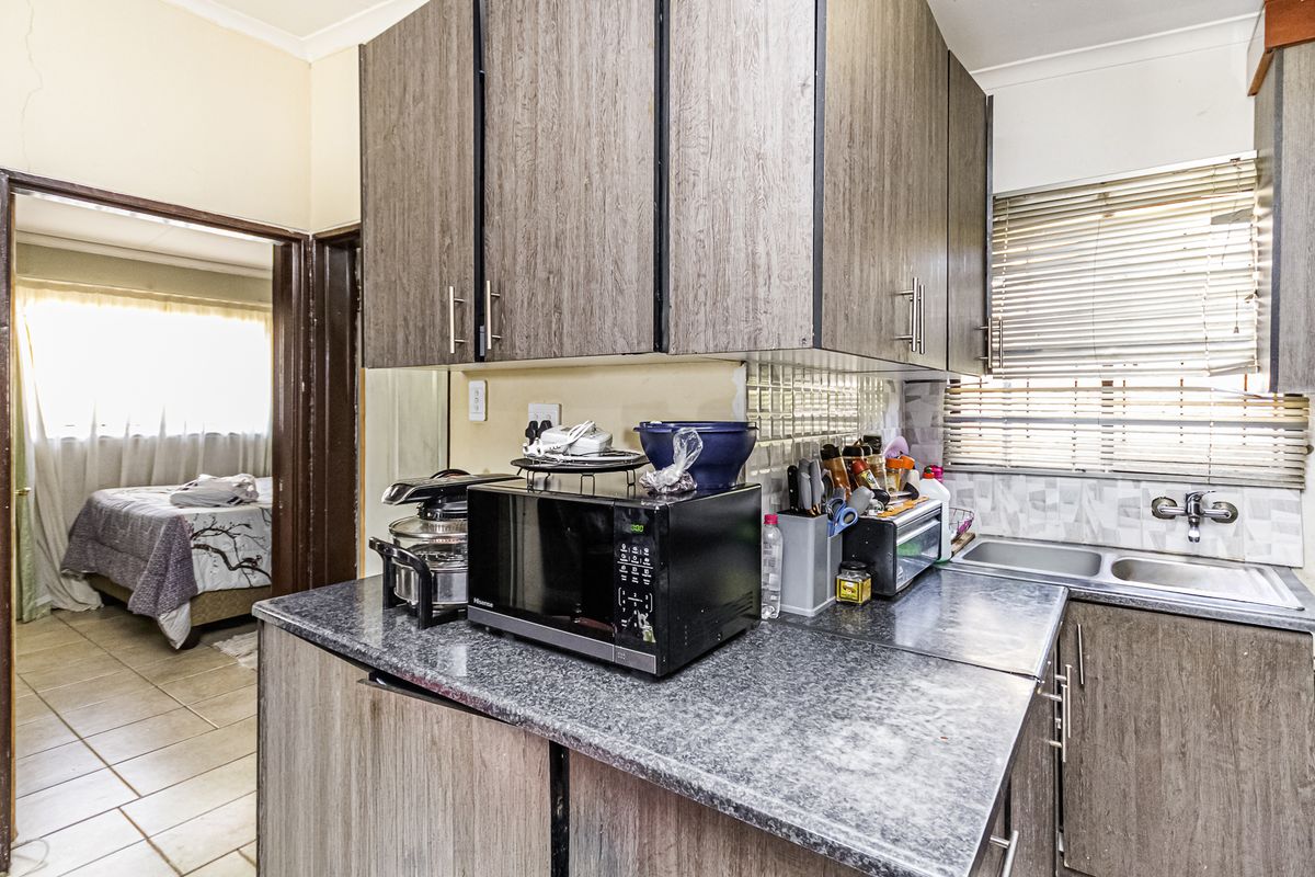 Compact kitchen featuring laminate cabinetry, granite-look countertops, a double bowl stainless steel sink, and tiled backsplash, with a view into the adjacent bedroom.