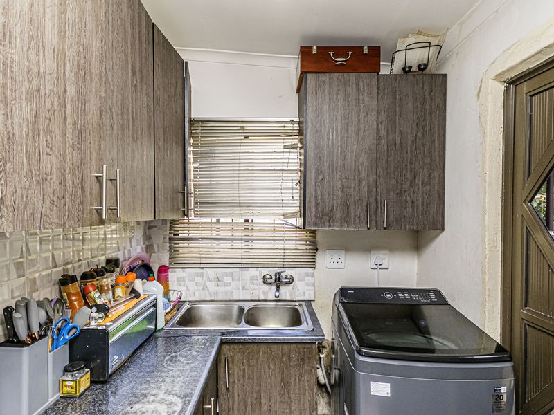 A functional laundry area featuring dark wood-look cabinetry, a double basin stainless steel sink, and a tiled backsplash.