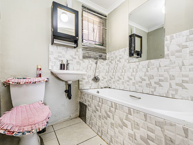A compact bathroom featuring a bathtub with tiled surround, wall-mounted basin, and toilet. The space would benefit from cosmetic updates to finishes and paint.