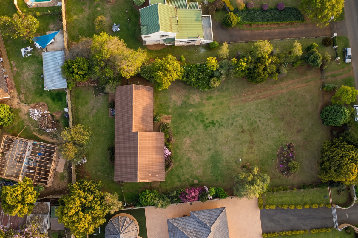 Aerial view of a residential property featuring a large garden, tiled roof dwelling, and an unfinished timber structure on the side.