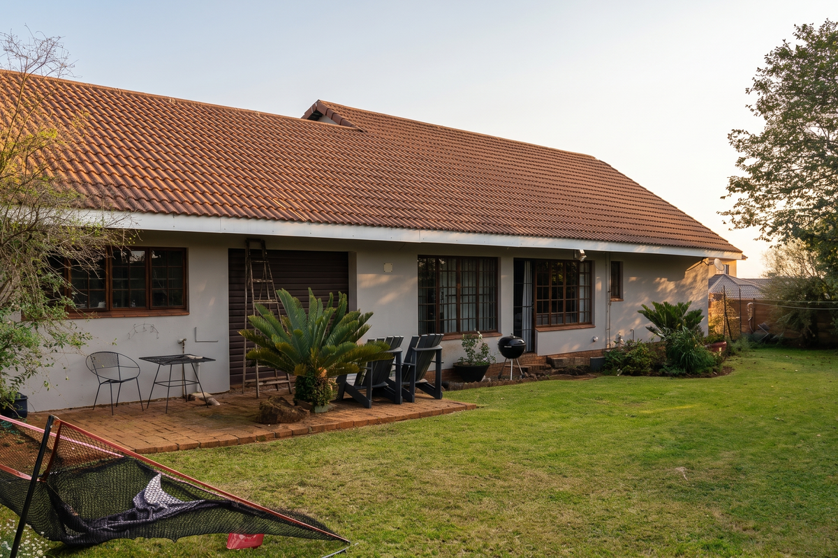 Rear view of the house featuring a tiled roof, brick patio area, and timber-framed windows overlooking a spacious garden.