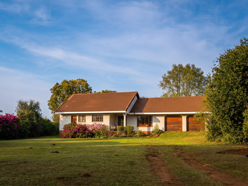 A well-maintained single-story residence featuring a tiled roof, double garage with wooden doors, and a spacious front garden.