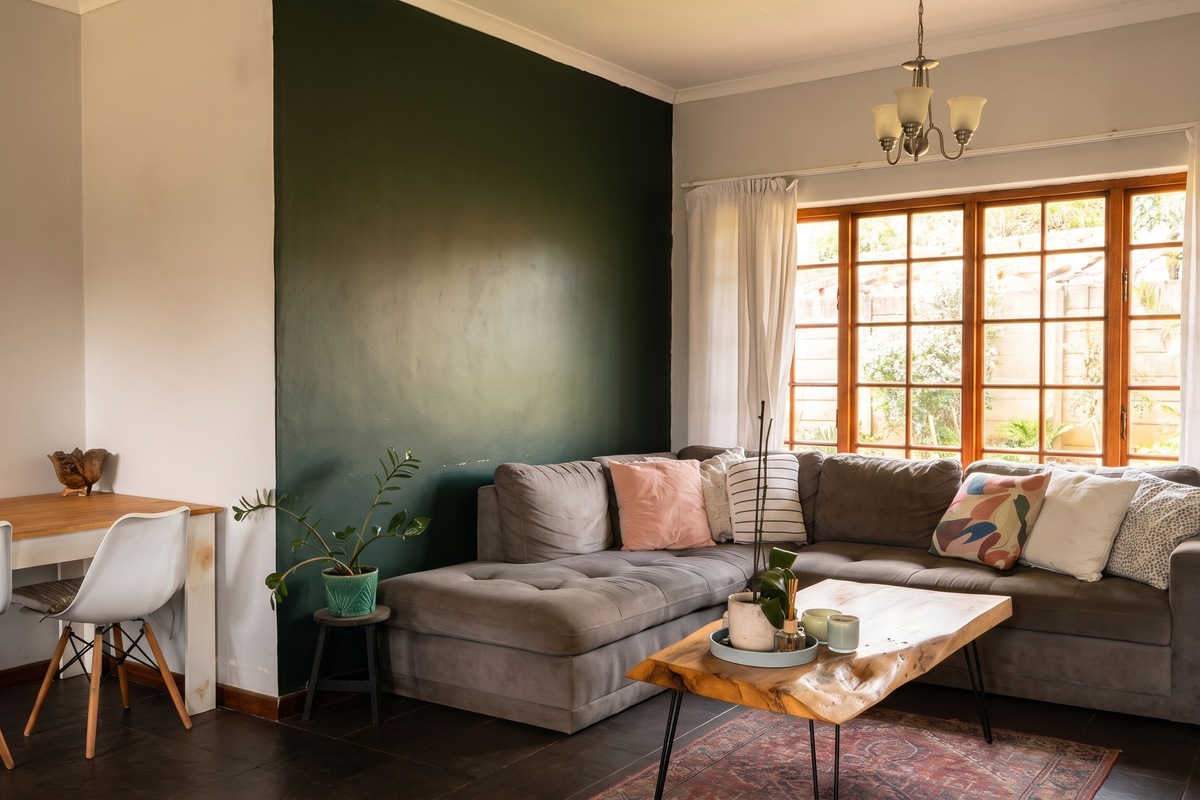 A comfortable living room featuring tiled flooring, a large window with wooden frames, and a feature wall, providing a bright and inviting space.