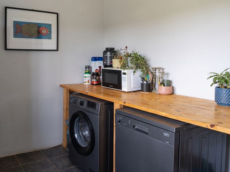 A functional laundry area featuring a solid wooden countertop with space for under-counter appliances and tiled flooring.