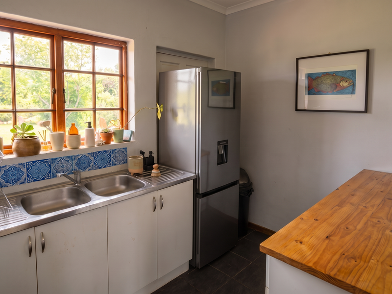 A functional scullery area featuring a double stainless steel sink, tiled splashback, timber countertop, and ample built-in cabinetry with a view of the garden.