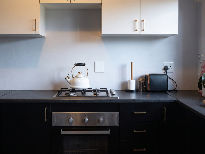 A modern kitchen featuring dark lower cabinetry, white upper cabinets, a gas hob, and a built-in oven with sleek hardware.
