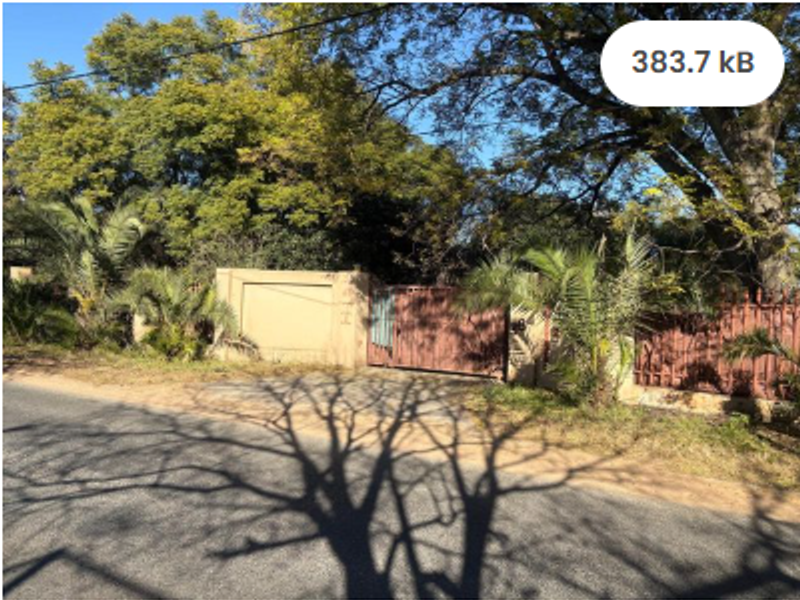 Front view of a residential property featuring a boundary wall, metal gate, and mature trees along the street frontage.