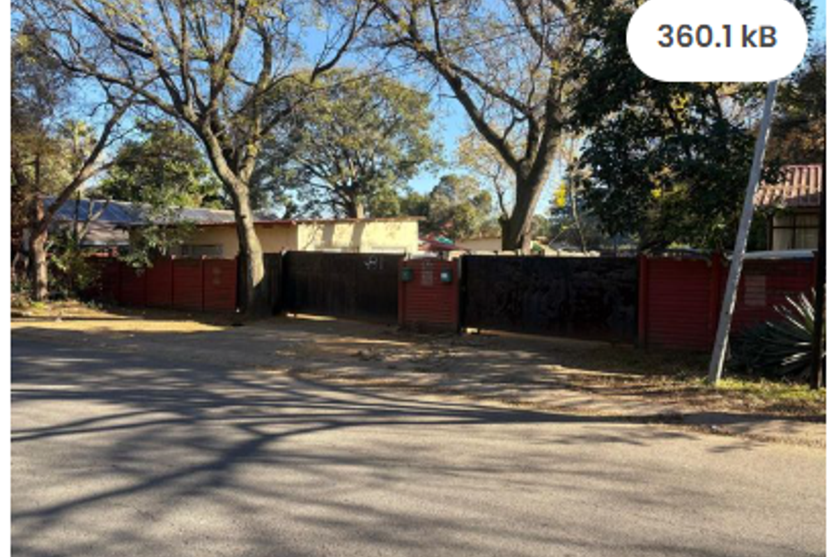 Street view of the property entrance featuring a gated driveway and perimeter wall surrounded by mature trees.