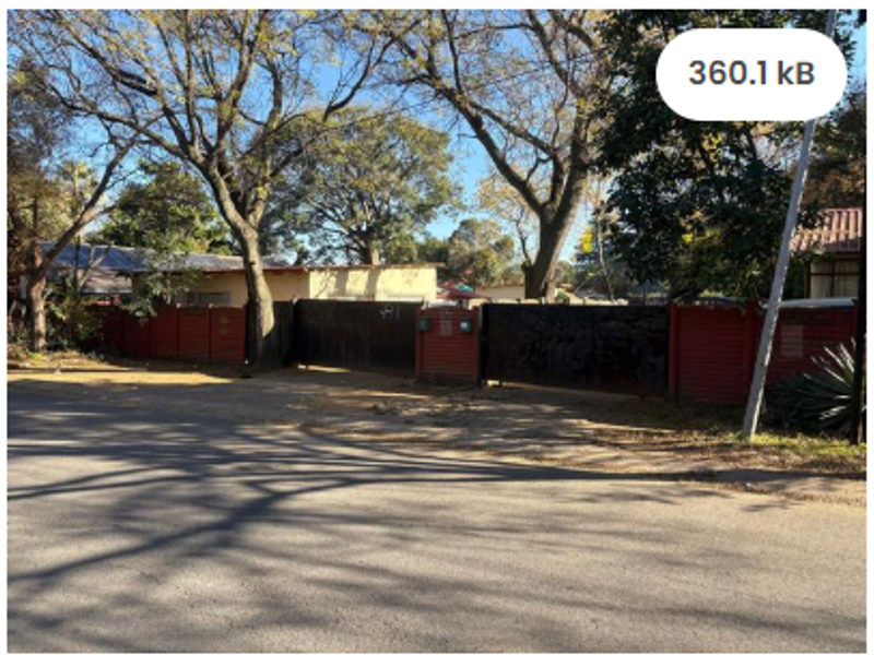 Street view of the property entrance featuring a gated driveway and perimeter wall surrounded by mature trees.