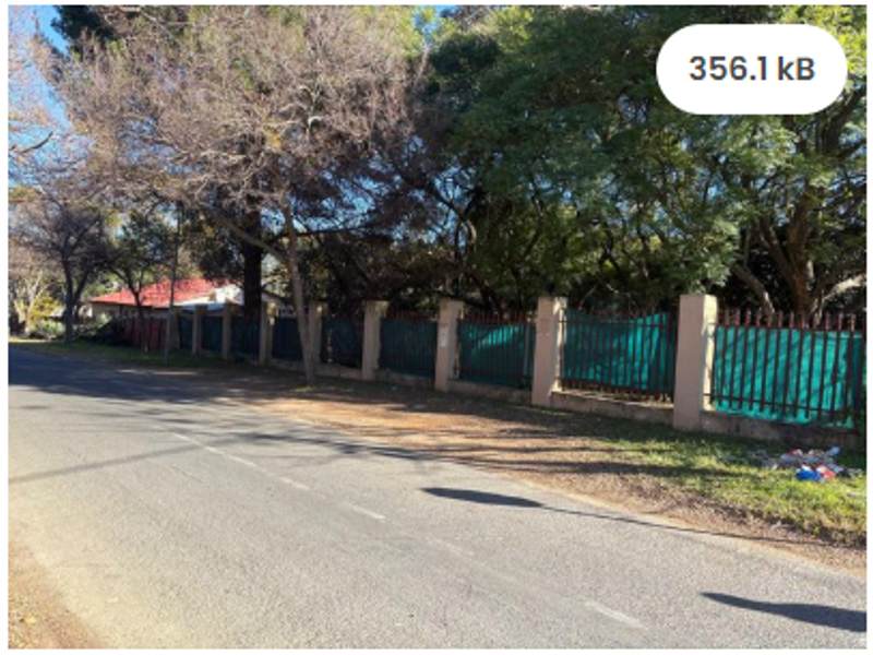 Street view of the residential property showing the perimeter wall and metal fencing along the roadside.