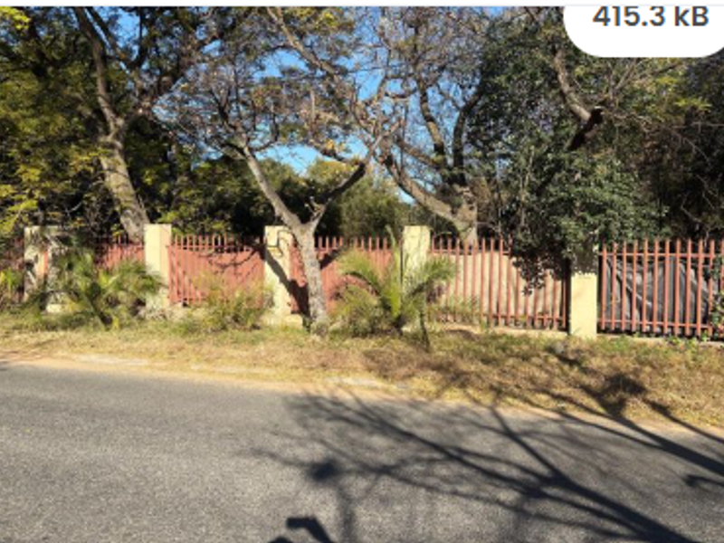 Street view of the property boundary featuring masonry pillars and metal perimeter fencing surrounded by mature trees.
