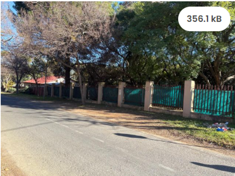 Street view of the property frontage featuring a perimeter wall with metal fencing and mature trees along the roadside.