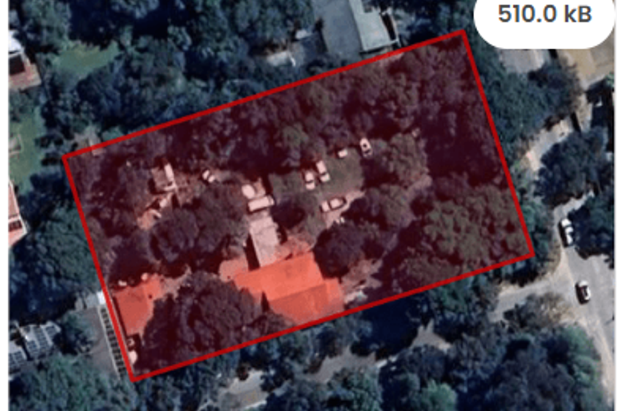 Aerial view of a residential plot featuring mature trees and existing structures, outlined in red for property boundary identification.