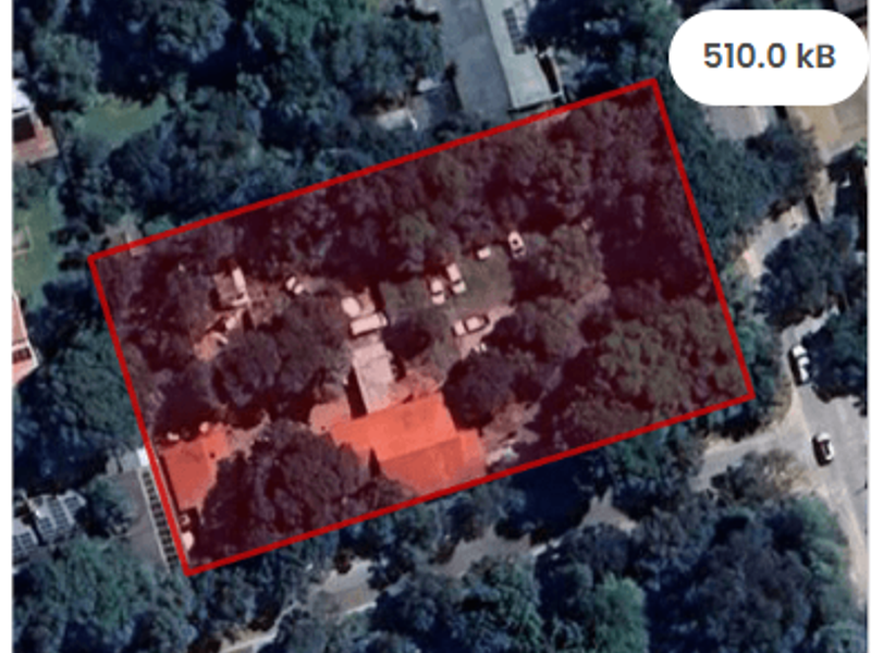 Aerial view of a residential plot featuring mature trees and existing structures, outlined in red for property boundary identification.