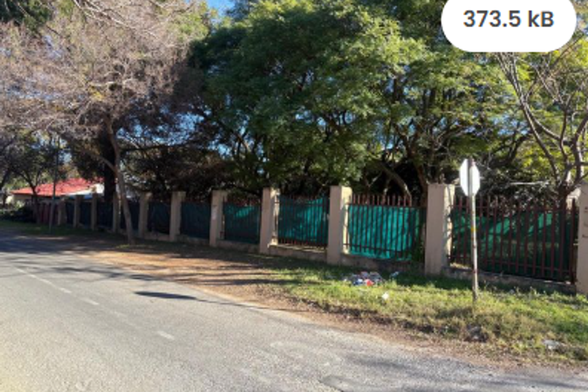 Street view of the residential property boundary featuring a masonry wall with metal palisade fencing and mature trees.