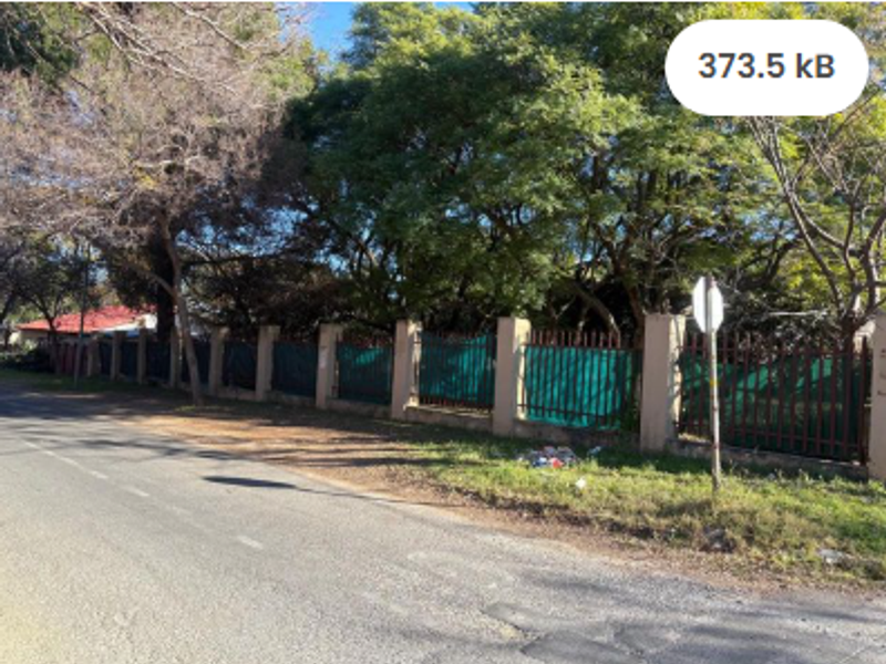 Street view of the residential property boundary featuring a masonry wall with metal palisade fencing and mature trees.