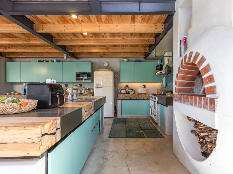 Modern industrial-style kitchen featuring exposed timber ceilings, steel beams, custom cabinetry, concrete flooring, and a unique built-in brick pizza oven.