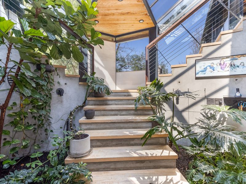 Modern architectural entrance featuring a concrete staircase with timber treads, glass ceiling, and exposed concrete walls, creating a bright and contemporary transition space.