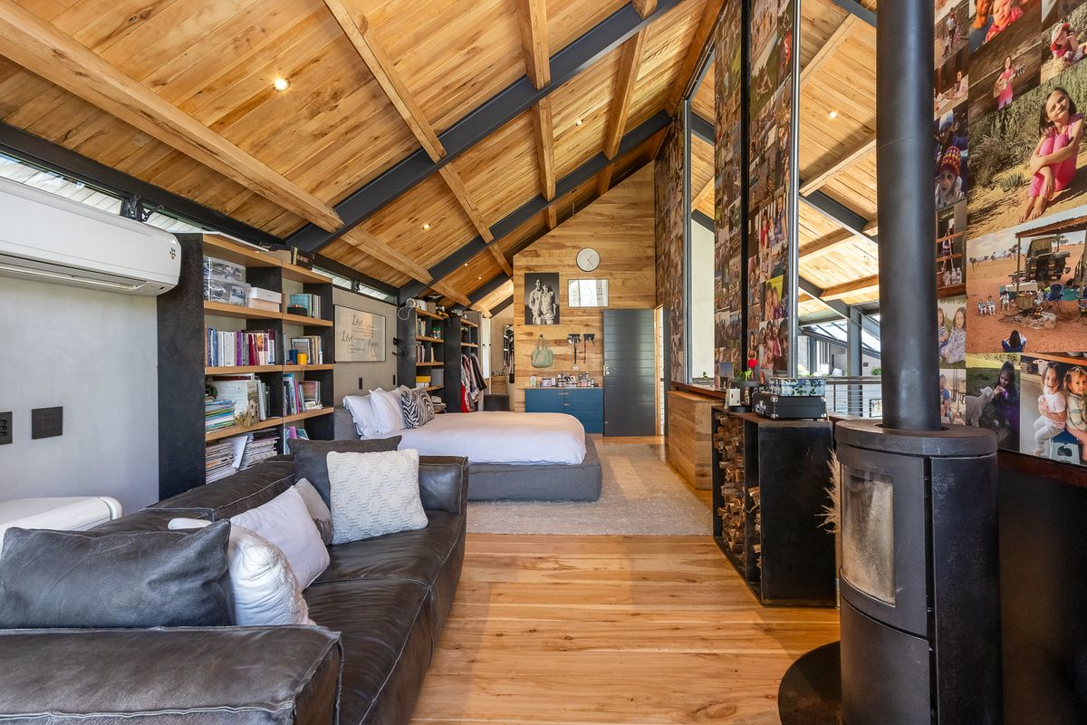 Spacious bedroom featuring high vaulted timber ceilings with exposed steel beams, a wood-burning fireplace, built-in shelving, and timber flooring.