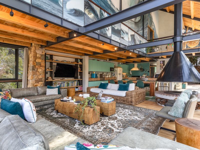 Spacious open-plan living and kitchen area featuring high timber ceilings, exposed steel beams, a striking suspended fireplace, and a stone feature wall.