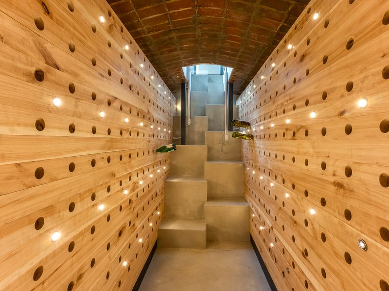 A sophisticated wine cellar featuring custom timber racking with integrated lighting, an exposed brick barrel vault ceiling, and a modern concrete staircase.
