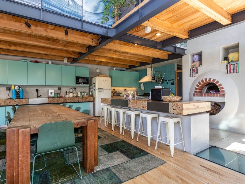 Spacious open-plan kitchen and dining area featuring exposed timber beams, steel structural elements, a built-in pizza oven, and modern cabinetry.