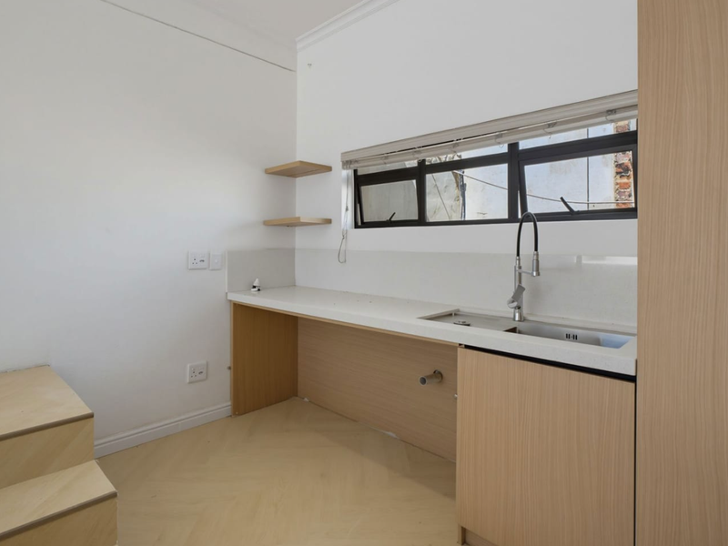 A modern, minimalist kitchen area featuring light wood cabinetry, stone countertops, an undermount sink, and floating shelves, finished with herringbone flooring.
