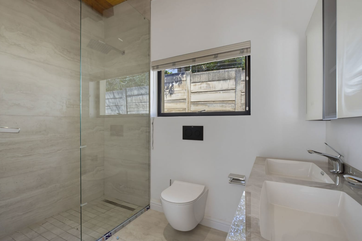 Modern bathroom featuring a spacious walk-in shower with glass screen, wall-mounted toilet, and a sleek dual vanity with stone countertop.