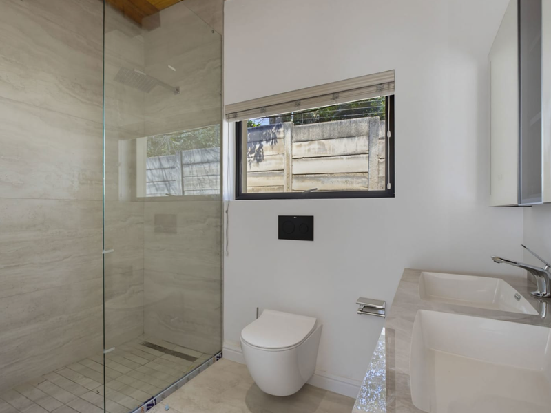 Modern bathroom featuring a spacious walk-in shower with glass screen, wall-mounted toilet, and a sleek dual vanity with stone countertop.