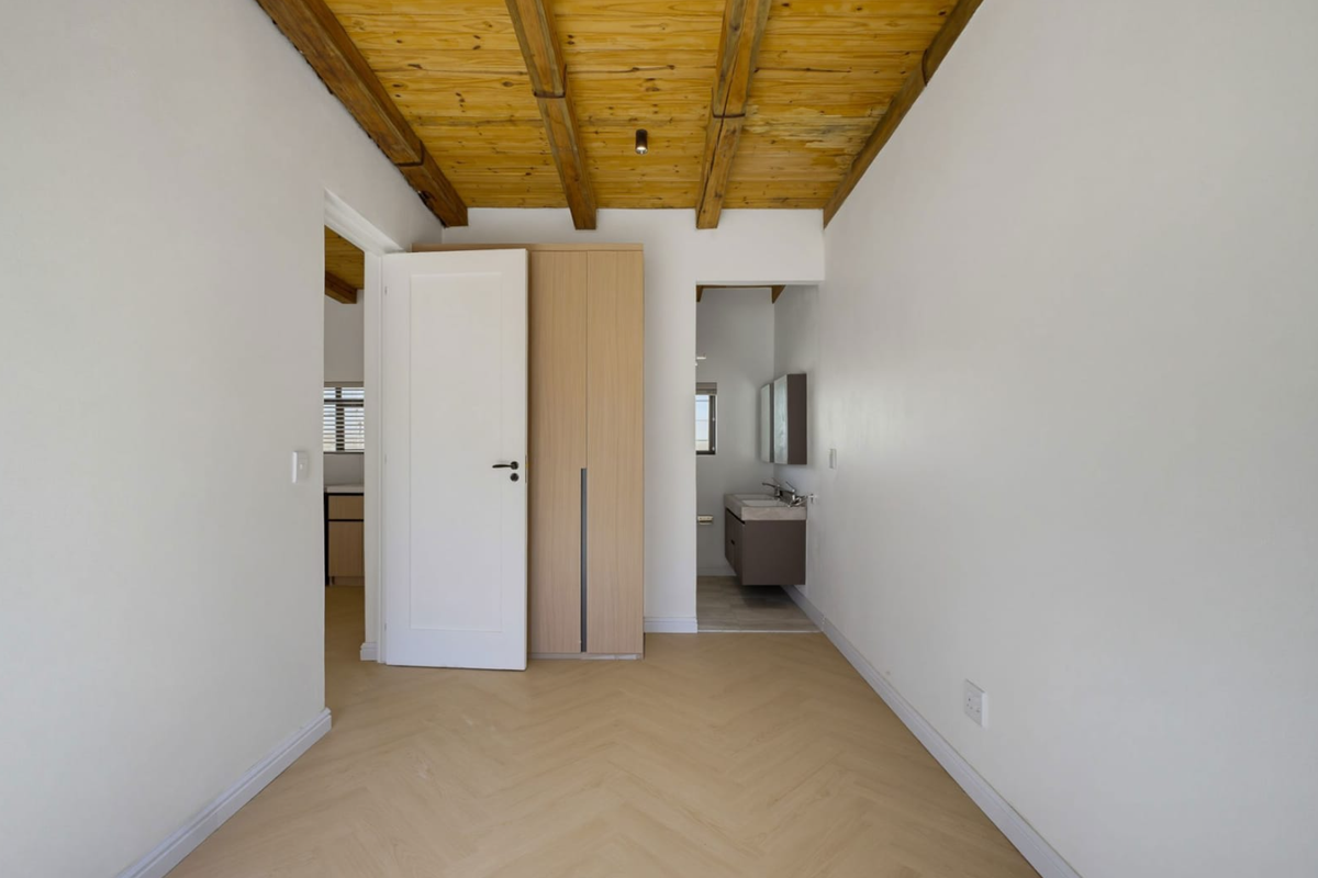 A bright, empty bedroom featuring exposed timber ceiling beams, herringbone flooring, a built-in wardrobe, and direct access to an en-suite bathroom.