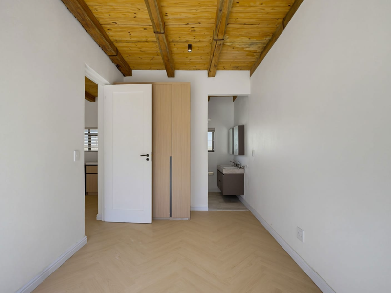 A bright, empty bedroom featuring exposed timber ceiling beams, herringbone flooring, a built-in wardrobe, and direct access to an en-suite bathroom.