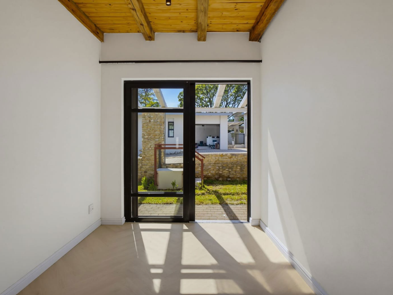A bright, empty living space featuring a warm timber beam ceiling, herringbone flooring, and a large sliding glass door opening to the rear garden.