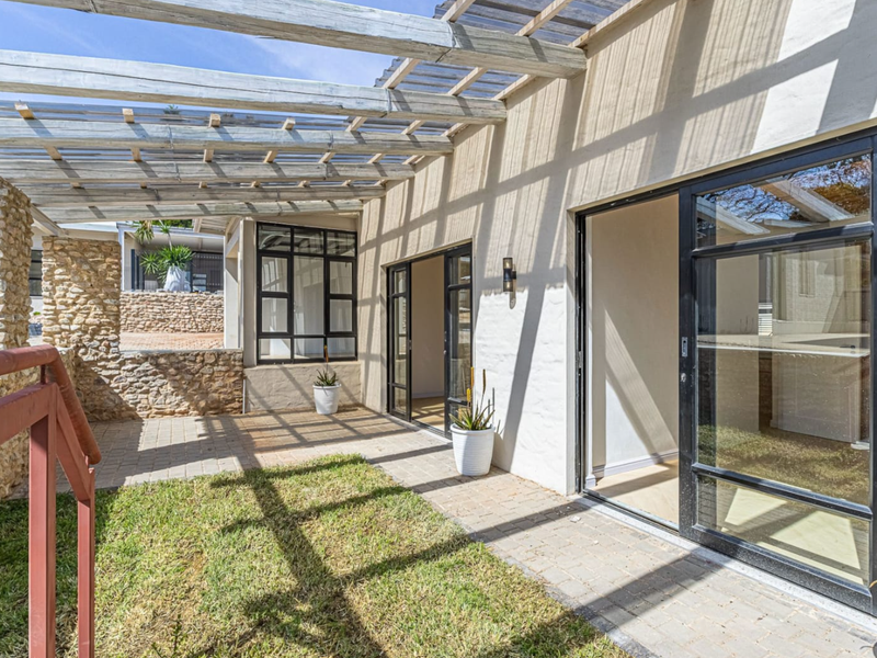 A covered patio area featuring a timber pergola, stone wall accents, and black aluminium sliding doors leading into the home.