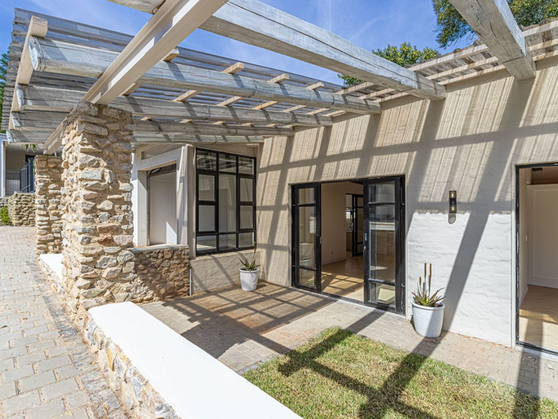 A covered patio area featuring a timber pergola, stone-clad pillar, and black-framed glass sliding doors providing seamless access to the interior living space.