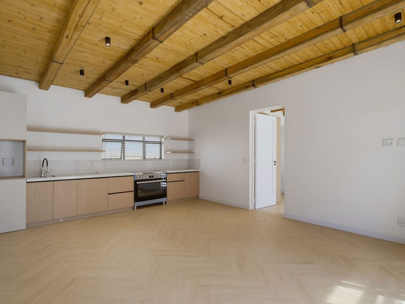 Modern open-plan kitchen featuring light wood cabinetry, herringbone flooring, and exposed timber ceiling beams, creating a bright and contemporary living space.